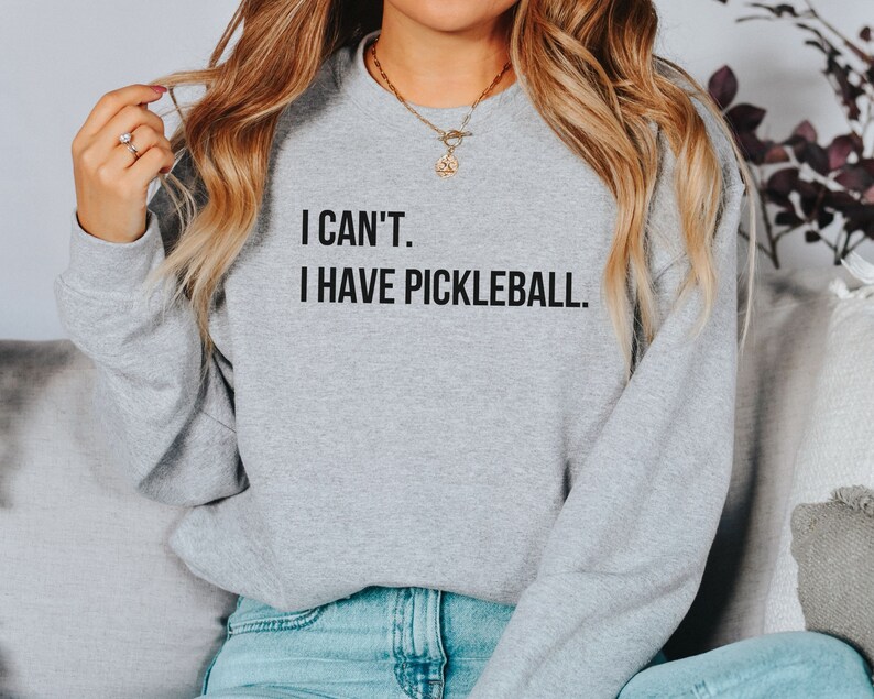 K&ouml;nnte beinhalten: Ein graues Sweatshirt mit dem Text "I can't. I have pickleball." auf der Vorderseite.
