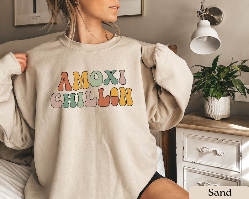 May include: A beige sweatshirt with the text "AMOXl CHILLlN" in colorful retro-style lettering.
