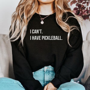 K&ouml;nnte beinhalten: Ein schwarzer Pullover mit dem Text "I CAN'T. I HAVE PICKLEBALL." in wei&szlig;en Buchstaben.
