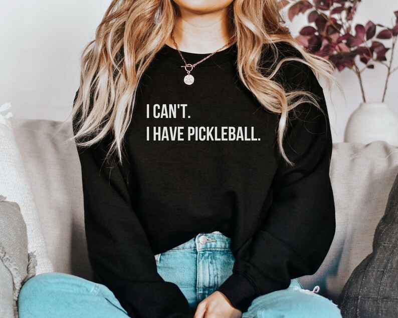 K&ouml;nnte beinhalten: Ein schwarzer Pullover mit dem Text "I CAN'T. I HAVE PICKLEBALL." in wei&szlig;en Buchstaben.
