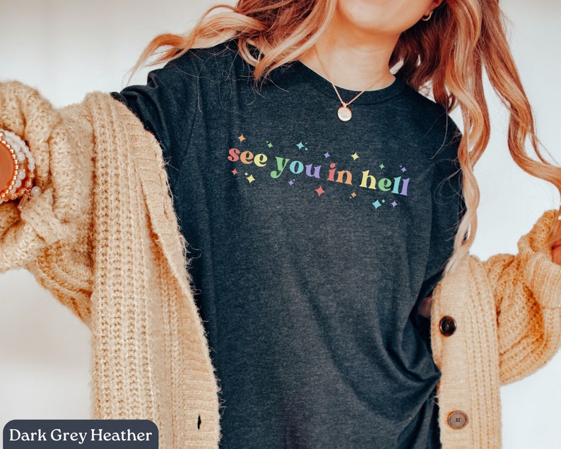 Puede incluir: Camiseta de color gris oscuro jaspeado con el texto "see you in hell" en colores arco&iacute;ris y peque&ntilde;as estrellas blancas.