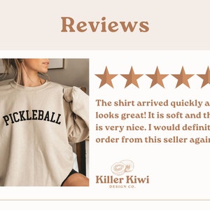 May include: A beige sweatshirt with the word "PICKLEBALL" printed in black on the front. The sweatshirt is being worn by a person. The image includes a five-star rating and a review that says "The shirt arrived quickly and it looks great! It is soft and the color is very nice. I would definitely order from this seller again!" The review is from Killer Kiwi Design Co.