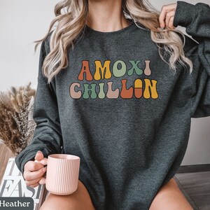 May include: A dark heather grey sweatshirt with the text "MOXI CHILLIN" in colorful retro-style lettering.