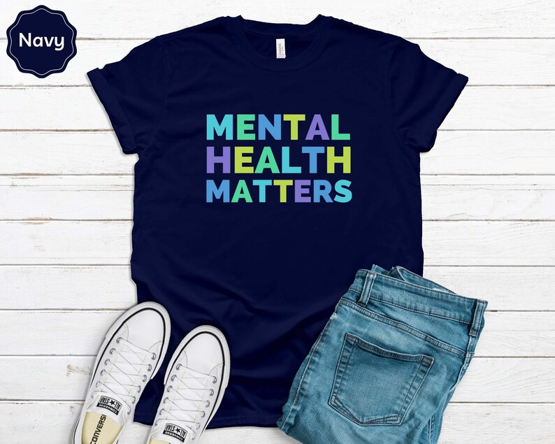 Puede incluir: Una camiseta azul marino con el texto "MENTAL HEALTH MATTERS" en colores arco&iacute;ris.