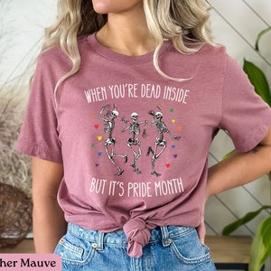 May include: Heather mauve t-shirt with a graphic of three skeletons dancing with rainbow colors and the text "When you're dead inside but it's pride month."