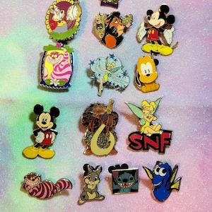 May include: A collection of 14 Disney character enamel pins. The pins feature characters like Mickey Mouse, Tinkerbell, Stitch, and the Cheshire Cat. The pins are all different colors and designs.
