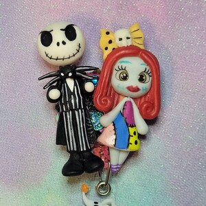 May include: A Nightmare Before Christmas themed badge reel featuring Jack Skellington, Sally, and Zero. The characters are made of polymer clay and are brightly colored. The reel is silver and has a clear plastic badge holder.