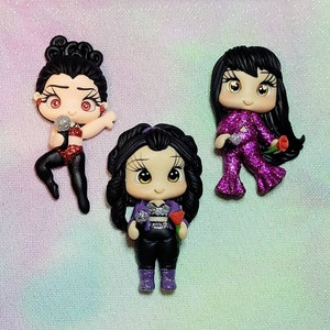 May include: Three handmade polymer clay figurines of women with black hair, wearing different outfits. The figurine on the left is wearing a red and black outfit and holding a microphone. The figurine in the middle is wearing a black and white outfit and holding a microphone and a red rose. The figurine on the right is wearing a purple and black outfit and holding a microphone and a red rose.