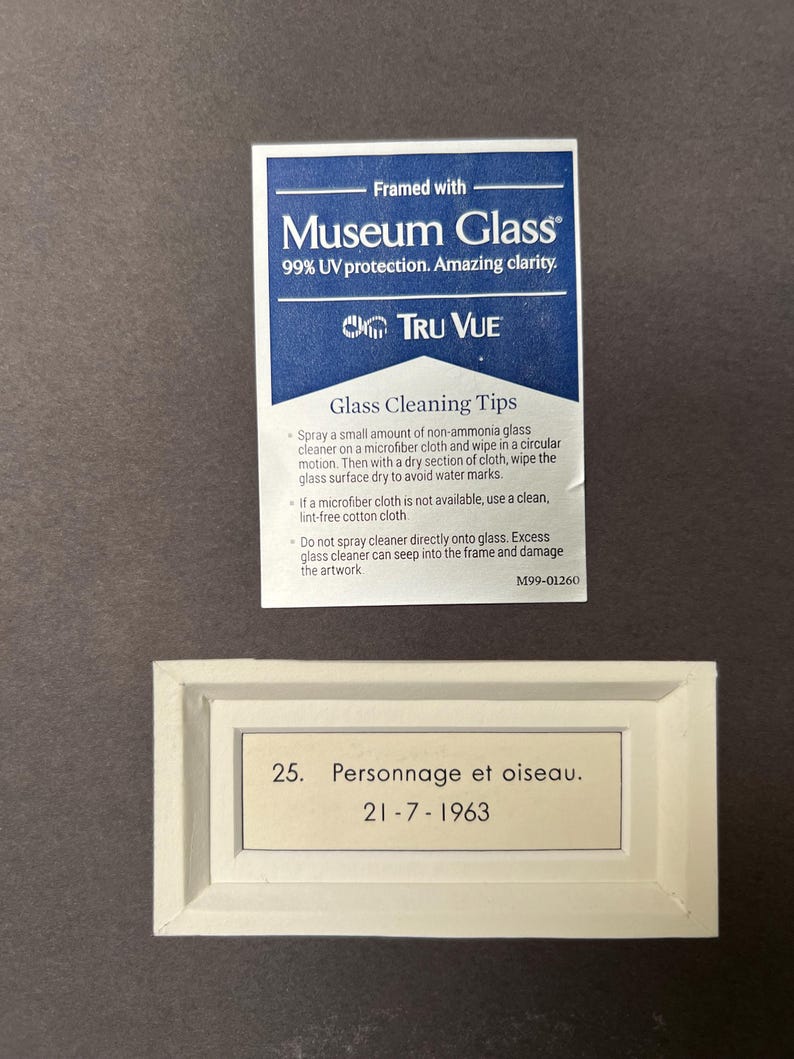 May include: A white framed label with black text that reads "25. Personnage et oiseau. 21-7-1963". The label is on a dark brown background.