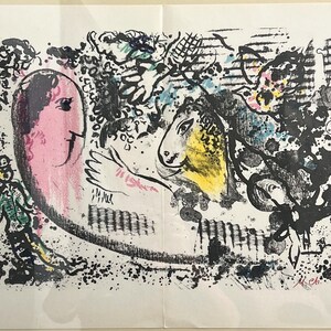 May include: Abstract art print featuring a pink face, a yellow horse head, and a figure in green. The artwork uses black, blue, and pink brushstrokes, with a signature in the lower right corner. The print is on white paper.