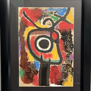 May include: Abstract art print with a colorful, geometric design. The print features a central circle with a black center and a white ring, surrounded by red, yellow, green, and blue shapes. The print is framed in black.