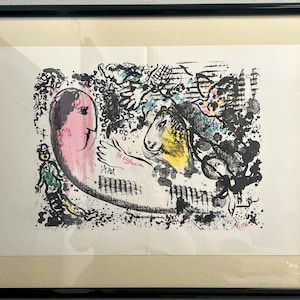 May include: Abstract art print in a black frame. The artwork features a pink figure with a face, a yellow horse, and various other figures and shapes in black, blue, and green. The print is on a white background.
