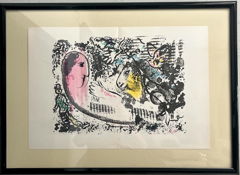 May include: Abstract art print in a black frame. The artwork features a pink figure with a face, a yellow horse, and various other figures and shapes in black, blue, and green. The print is on a white background.