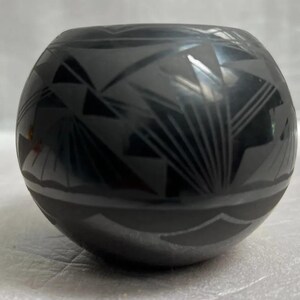 Könnte beinhalten: Schwarze Töpferschale mit geometrischem Muster. Die Schale ist rund und hat eine glatte, glänzende Oberfläche.
