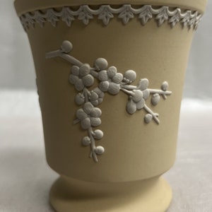 Może przedstawiać: Jasnożółty ceramiczny wazon z białym wzorem kwiatowym. Wazon ma falowany brzeg i rozszerzającą się podstawę.