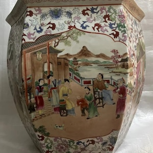 Könnte beinhalten: Ein weißer Porzellantopf mit einem mehrfarbigen Blumendesign und einer Szene von Menschen in einem chinesischen Garten. Der Topf ist achteckig und hat eine breite Öffnung.