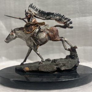 May include: A silver and bronze sculpture of a Native American warrior riding a horse. The warrior is wearing a feathered headdress and holding a spear. The sculpture is titled "The Final Charge" and is signed "C.F. Padgett".