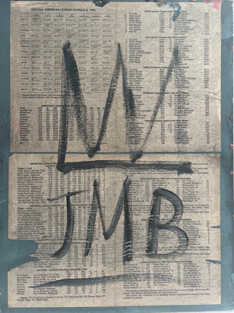 May include: Artwork featuring a vintage baseball schedule from 1983, overlaid with bold black graffiti-style lettering. The text "M JMB" is prominently displayed, adding an urban art aesthetic to the aged paper background.