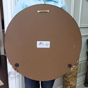 Puede incluir: Parte trasera de una gran obra de arte mural redonda. La pieza tiene un respaldo marr&oacute;n, un borde negro y un colgador de sierra met&aacute;lica. Se ven dos patas de goma negras. Una pegatina blanca con el texto "ART DECORS" y "LOVE" est&aacute; adherida.