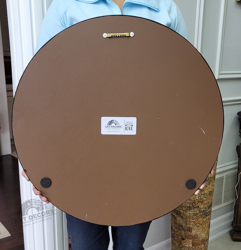 Puede incluir: Parte trasera de una gran obra de arte mural redonda. La pieza tiene un respaldo marr&oacute;n, un borde negro y un colgador de sierra met&aacute;lica. Se ven dos patas de goma negras. Una pegatina blanca con el texto "ART DECORS" y "LOVE" est&aacute; adherida.