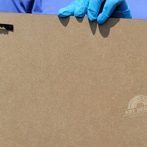 Puede incluir: Parte trasera de un panel de arte rectangular de color marr&oacute;n claro, con dos colgadores de dientes de sierra negros. El panel tiene un logotipo "ART DECORS" en la esquina inferior derecha.