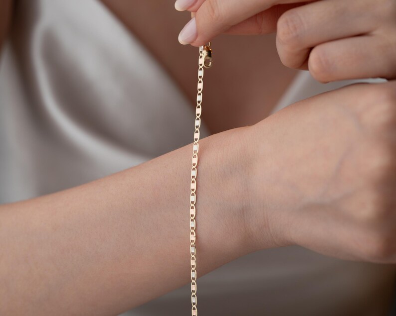 Puede incluir: Una delicada pulsera de cadena de oro que presenta una serie de eslabones planos de forma ovalada conectados en un patr&oacute;n repetitivo. La pulsera se asegura con un peque&ntilde;o cierre de mosquet&oacute;n funcional en la parte superior, con un acabado pulido.