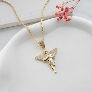 May include: A gold-toned necklace featuring a pendant shaped like a cherub with outstretched wings. The pendant is embellished with small, clear, sparkling stones covering the wings and the bail. The chain is a twisted rope style in gold metal.