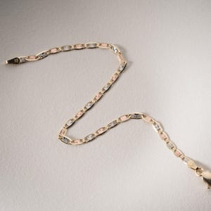 Puede incluir: Una pulsera de cadena de oro tricolor con eslabones ovalados alternos en oro amarillo, rosa y blanco. Los eslabones tienen un acabado texturizado tallado en diamante que refleja la luz. La pulsera incluye un cierre de mosquet&oacute;n.