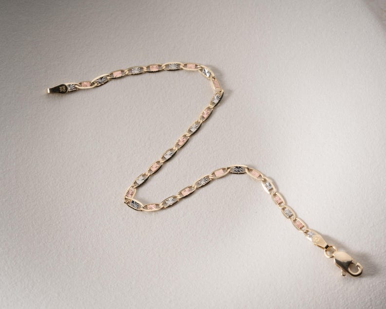 Puede incluir: Una pulsera de cadena de oro tricolor con eslabones ovalados alternos en oro amarillo, rosa y blanco. Los eslabones tienen un acabado texturizado tallado en diamante que refleja la luz. La pulsera incluye un cierre de mosquet&oacute;n.