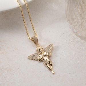 May include: A gold-toned necklace featuring a pendant shaped like a cherub with outstretched wings. The cherub figure is adorned with small, clear pav&eacute;-set stones on the wings and the bail, while the chain is a twisted rope style design.