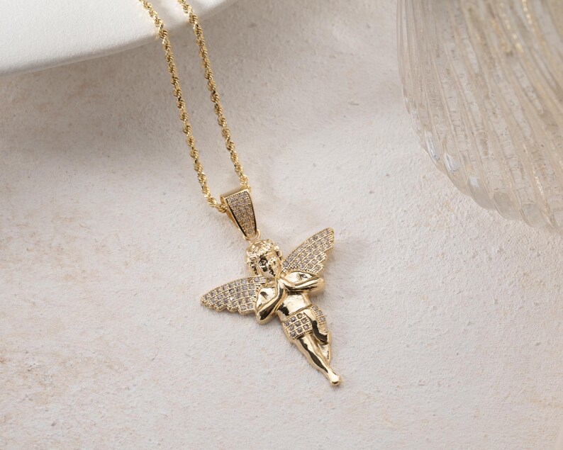 May include: A gold-toned necklace featuring a pendant shaped like a cherub with outstretched wings. The cherub figure is adorned with small, clear pav&eacute;-set stones on the wings and the bail, while the chain is a twisted rope style design.
