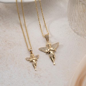May include: Two gold-toned necklaces featuring angel pendants with outstretched wings. Each pendant is embellished with small, clear, sparkling stones on the wings and body. The necklaces hang from thin, delicate gold-colored metal chains.