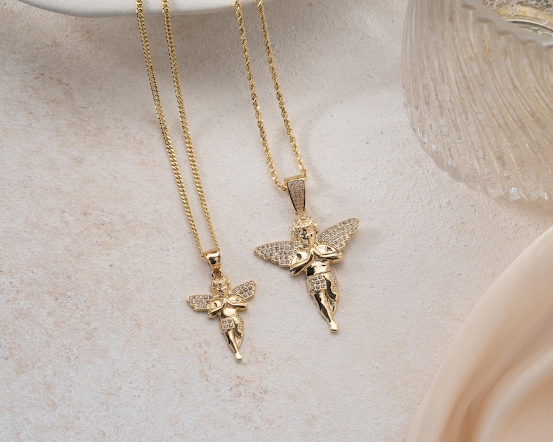 May include: Two gold-toned necklaces featuring angel pendants with outstretched wings. Each pendant is embellished with small, clear, sparkling stones on the wings and body. The necklaces hang from thin, delicate gold-colored metal chains.