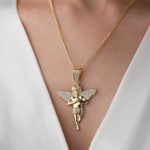 May include: A gold-toned necklace featuring a pendant shaped like a cherub with wings outstretched and hands pressed together in prayer. The cherub's wings and the pendant's bail are encrusted with small, clear, sparkling stones, while the chain is a link style.