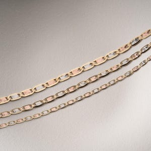 Puede incluir: Tres cadenas de oro de diferentes grosores dispuestas en diagonal. Cada cadena presenta un patr&oacute;n repetitivo de eslabones ovalados en tonos oro amarillo, blanco y rosa, con superficies texturizadas y facetadas que reflejan la luz sobre los eslabones.