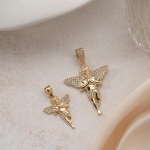 May include: Two gold-toned angel pendants featuring pav&eacute;-set clear stones on the wings and lower garments. Each pendant depicts a cherub figure with hands clasped in a prayer position, suspended from a small integrated bail at the top of the head.