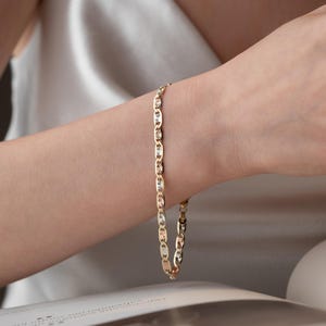 Puede incluir: Una pulsera de cadena dorada que presenta una serie de eslabones ovalados con un patr&oacute;n texturizado similar a un rayo de sol en cada segmento. La pulsera tiene un acabado pulido y un dise&ntilde;o repetitivo que alterna superficies met&aacute;licas lisas y grabadas.