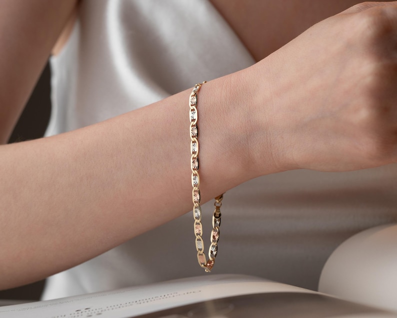 Puede incluir: Una pulsera de cadena dorada que presenta una serie de eslabones ovalados con un patr&oacute;n texturizado similar a un rayo de sol en cada segmento. La pulsera tiene un acabado pulido y un dise&ntilde;o repetitivo que alterna superficies met&aacute;licas lisas y grabadas.