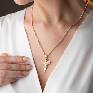 May include: A gold-toned rope chain necklace featuring a small, detailed angel pendant. The angel figure has outstretched wings and is embellished with small, clear, sparkling stones across its surface, suspended from a simple gold-toned bail.