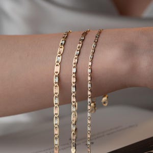 Puede incluir: Tres delicadas pulseras de cadena de oro con un dise&ntilde;o de eslabones marineros. Cada eslab&oacute;n alterna entre acabados de oro amarillo pulido, oro blanco texturizado y oro rosa, creando una apariencia met&aacute;lica multicolor en las tres cadenas.