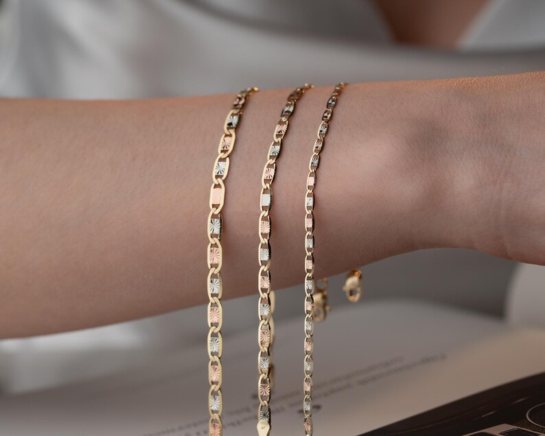 Puede incluir: Tres delicadas pulseras de cadena de oro con un dise&ntilde;o de eslabones marineros. Cada eslab&oacute;n alterna entre acabados de oro amarillo pulido, oro blanco texturizado y oro rosa, creando una apariencia met&aacute;lica multicolor en las tres cadenas.