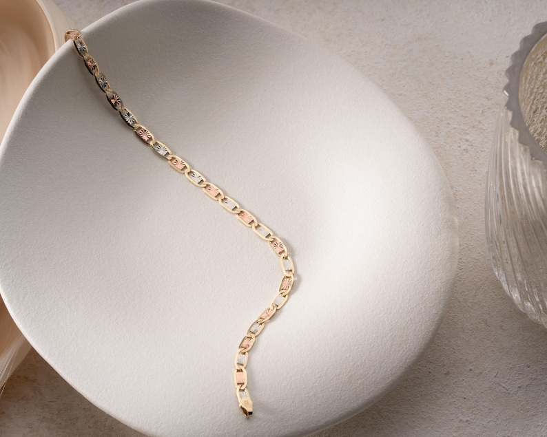 Puede incluir: Una pulsera de cadena de oro tricolor con eslabones ovalados y rectangulares texturizados que se alternan en tonos de oro amarillo, rosa y blanco. La pulsera tiene un acabado pulido con detalles grabados en los segmentos rectangulares.