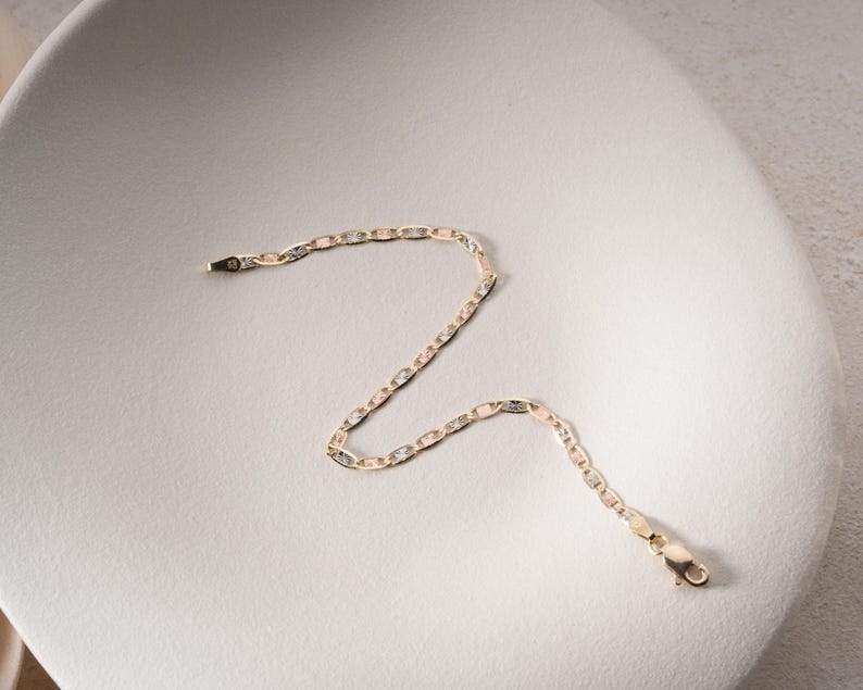 Puede incluir: Una delicada pulsera de cadena con eslabones ovalados y rectangulares alternos en un dise&ntilde;o de metal tricolor en tonos oro amarillo, rosa y blanco. La pulsera incluye un cierre de mosquet&oacute;n seguro en un extremo y una peque&ntilde;a anilla.