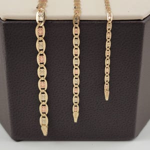 May include: Three gold chains with a textured design. The chains are different lengths and are displayed on a brown surface.