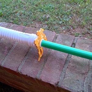 Puede incluir: Un juguete de sable de luz blanco y verde con un conector de plástico amarillo. El sable de luz está hecho de plástico y tiene una superficie texturizada.