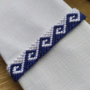 May include: A white fabric with a blue and white friendship bracelet with a geometric pattern.