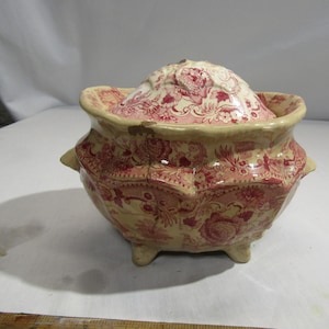 Könnte beinhalten: Eine antike, überdachte Keramikschale mit einem roten und weißen Blumenmuster. Die Schale hat drei Füße und einen Deckel mit einem Blumendesign.