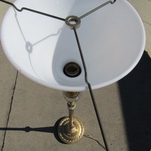 May include: A gold-colored lamp base with a white lampshade. The lampshade is attached to the base with a metal frame.