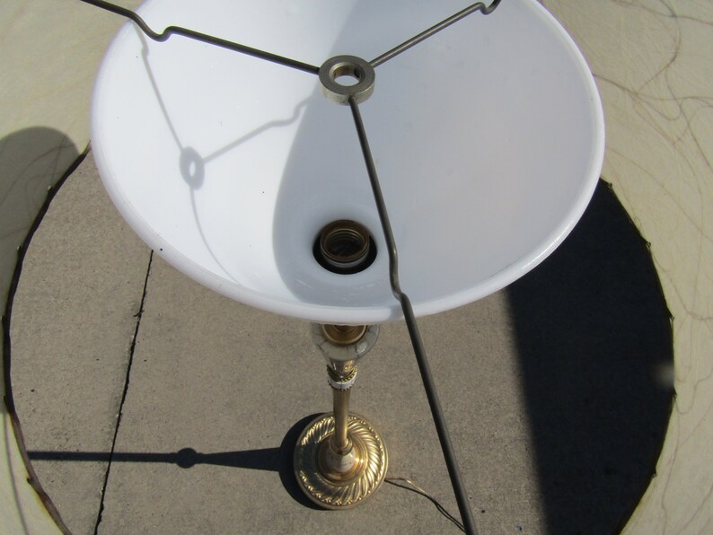 May include: A gold-colored lamp base with a white lampshade. The lampshade is attached to the base with a metal frame.