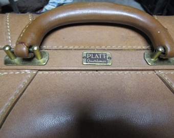 May include: A brown leather suitcase with a brass handle and a brass nameplate that reads "Platt Guardsman".